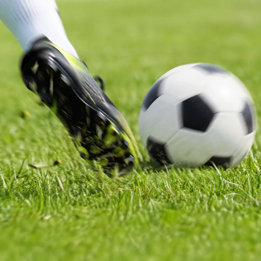 Close up shot of a football being kicked on green grass pitch, soft motion blur