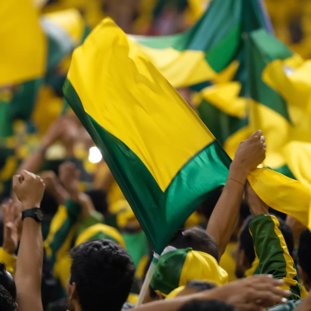 Close up shot of football fans waving yellow and green flags in a stadium crowd,