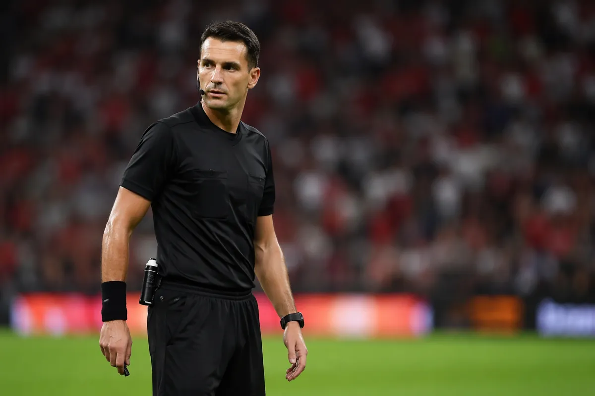 Professional football referee in black uniform standing on green football pitch under brig