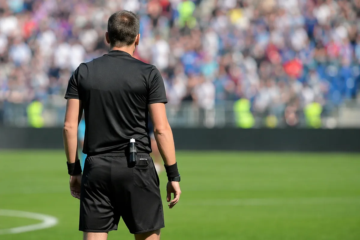 Professional football referee standing on a green soccer field, blurred background of stad