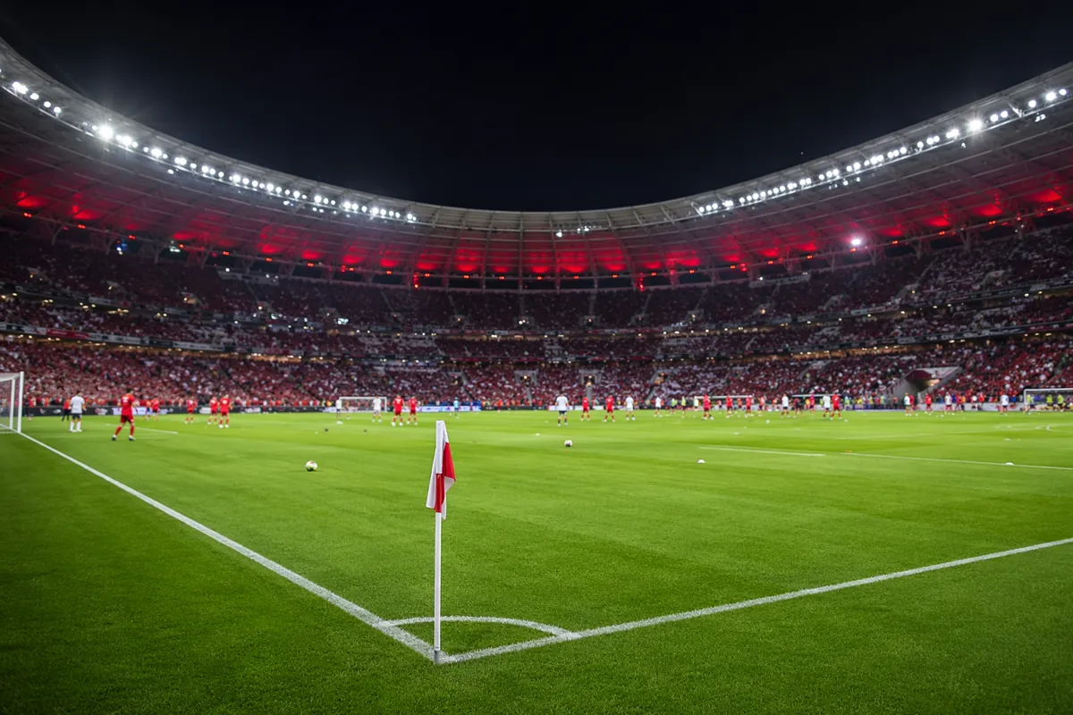 Wide shot of a professional football pitch under bright stadium floodlights, blurry player
