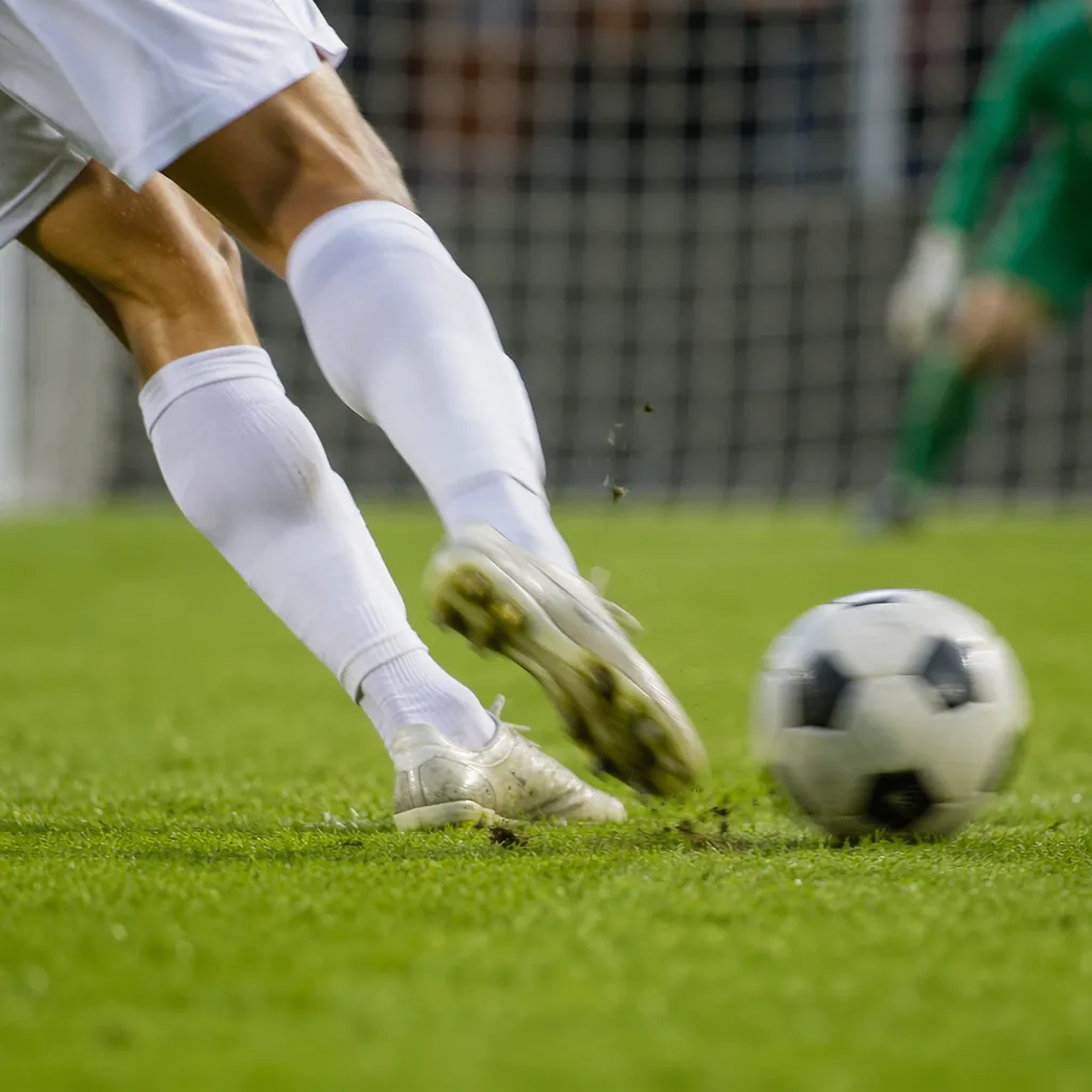 Close-up shot of a football player's lower body kicking a football from the pena