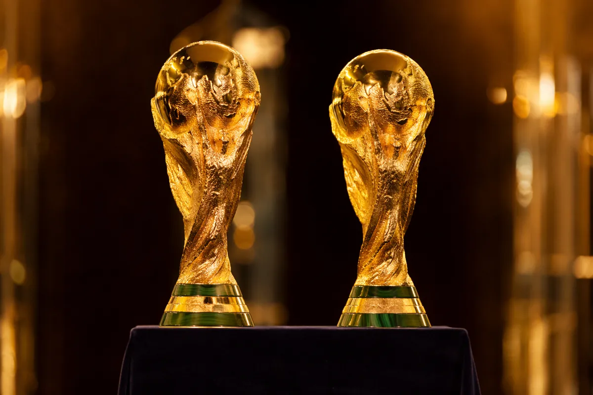 Two classic FIFA World Cup trophies placed side by side on a dark velvet display stand, so